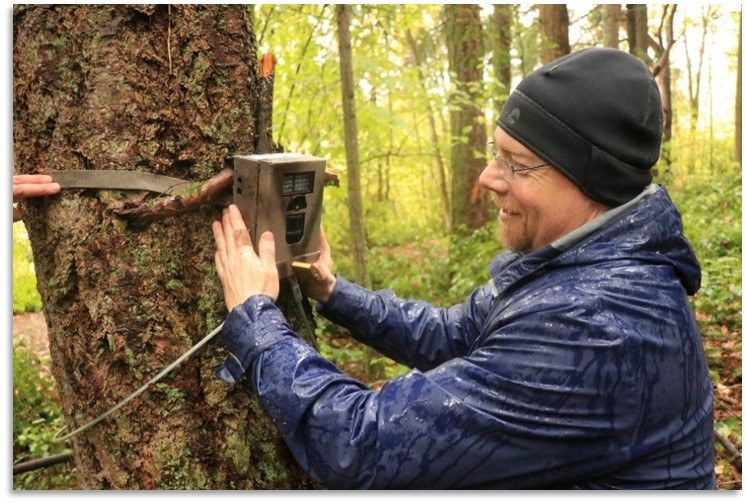 man attaching camera to tree