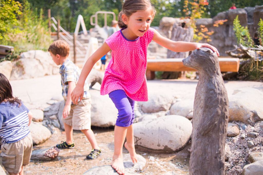Kids-Trek-girl-in-stream-with-otter-statue